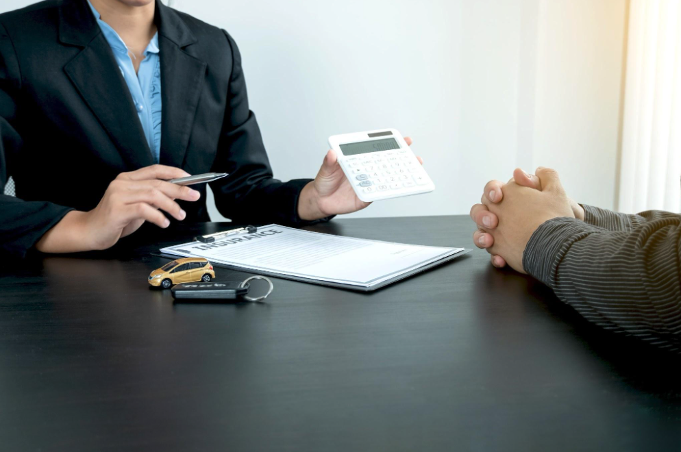 Insurance agent explaining auto insurance coverage and costs to a client during a policy consultation, with car keys and insurance paperwork on the desk.