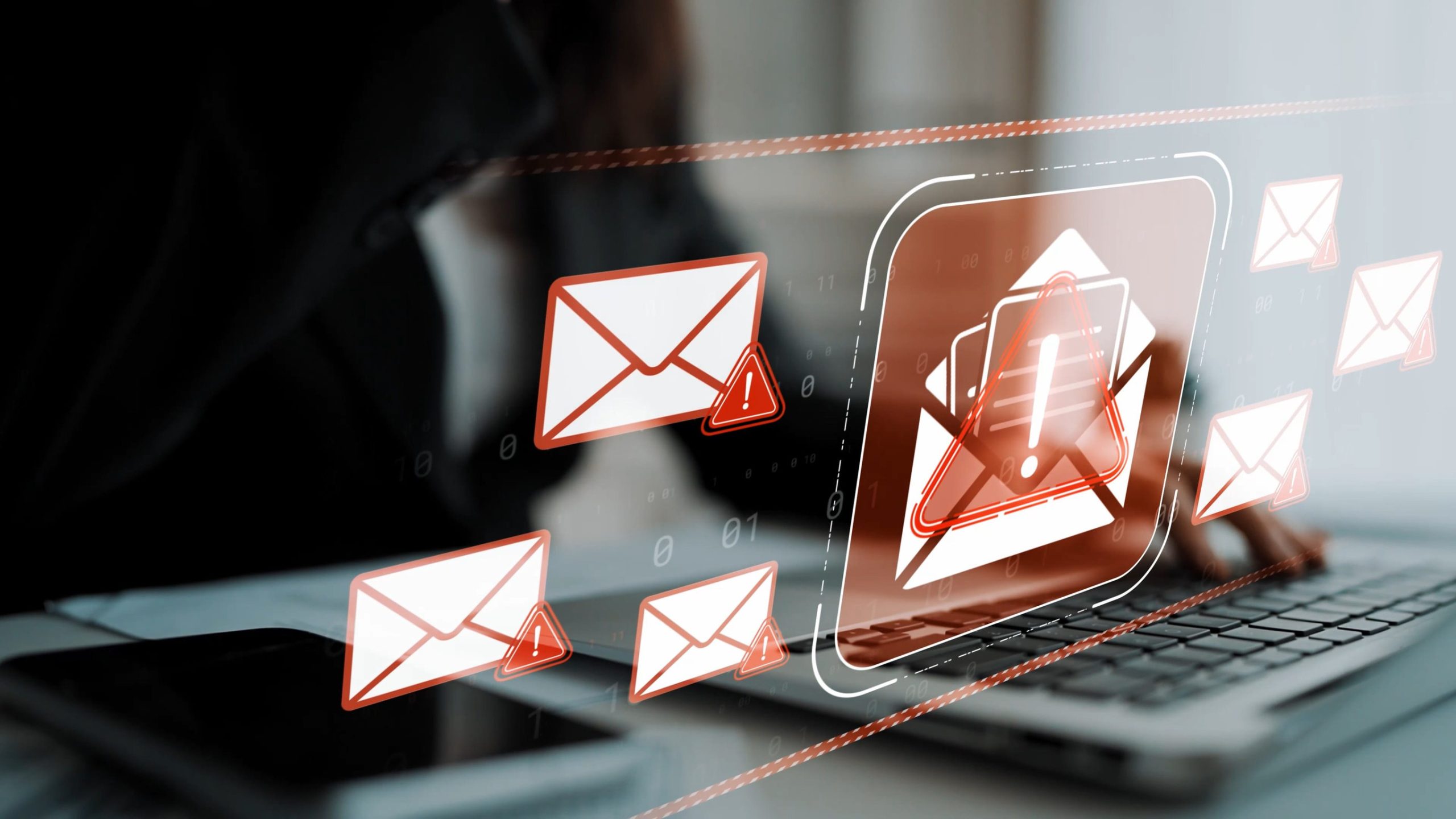 A person works on a laptop while warning icons appear over multiple email symbols, illustrating a phishing attack or suspicious email activity targeting a business computer system.